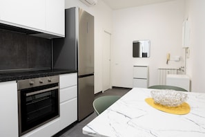 A modern kitchen with white cabinets, a stainless steel refrigerator, a built-in oven, and a marble countertop. - Kobogaisha (Rome)