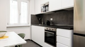 Cozinha moderna com armários brancos, bancada preta e eletrodomésticos de aço inoxidável.