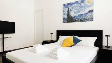 A hotel room with a bed, white linens, a painting of a night sky, and two nightstands with lamps.
