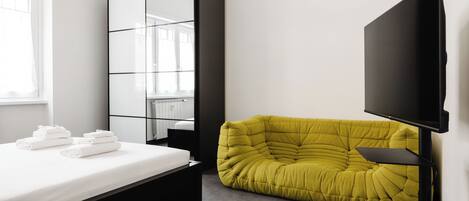 A modern bedroom with a bed, a large mirror, a yellow sofa, and a flat-screen TV.
