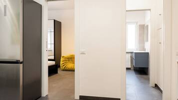 A modern kitchen with a built-in refrigerator, a dining area with a yellow chair, and a hallway leading to a bathroom.