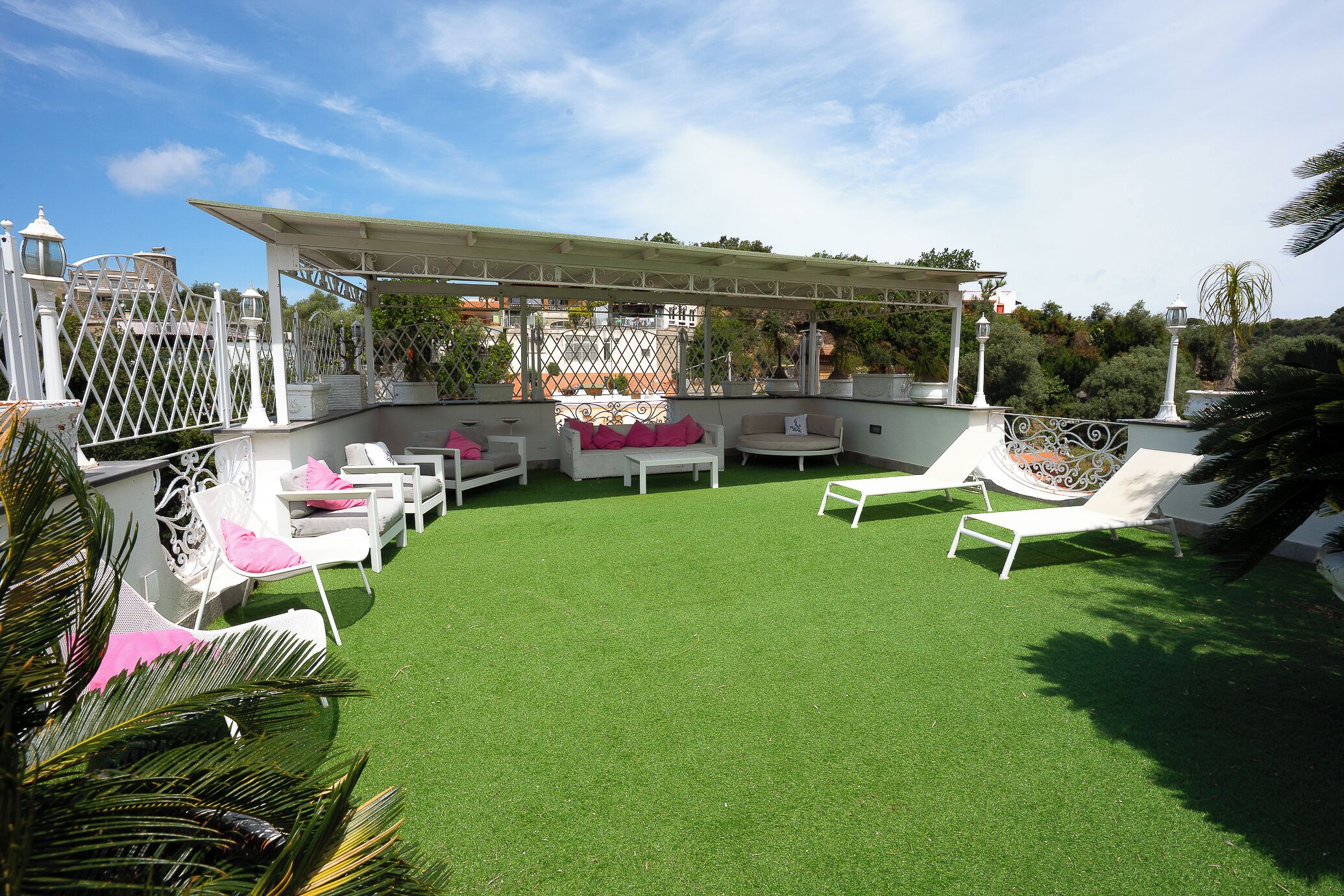Terraza en la azotea con césped artificial, mobiliario exterior blanco y una pérgola.
