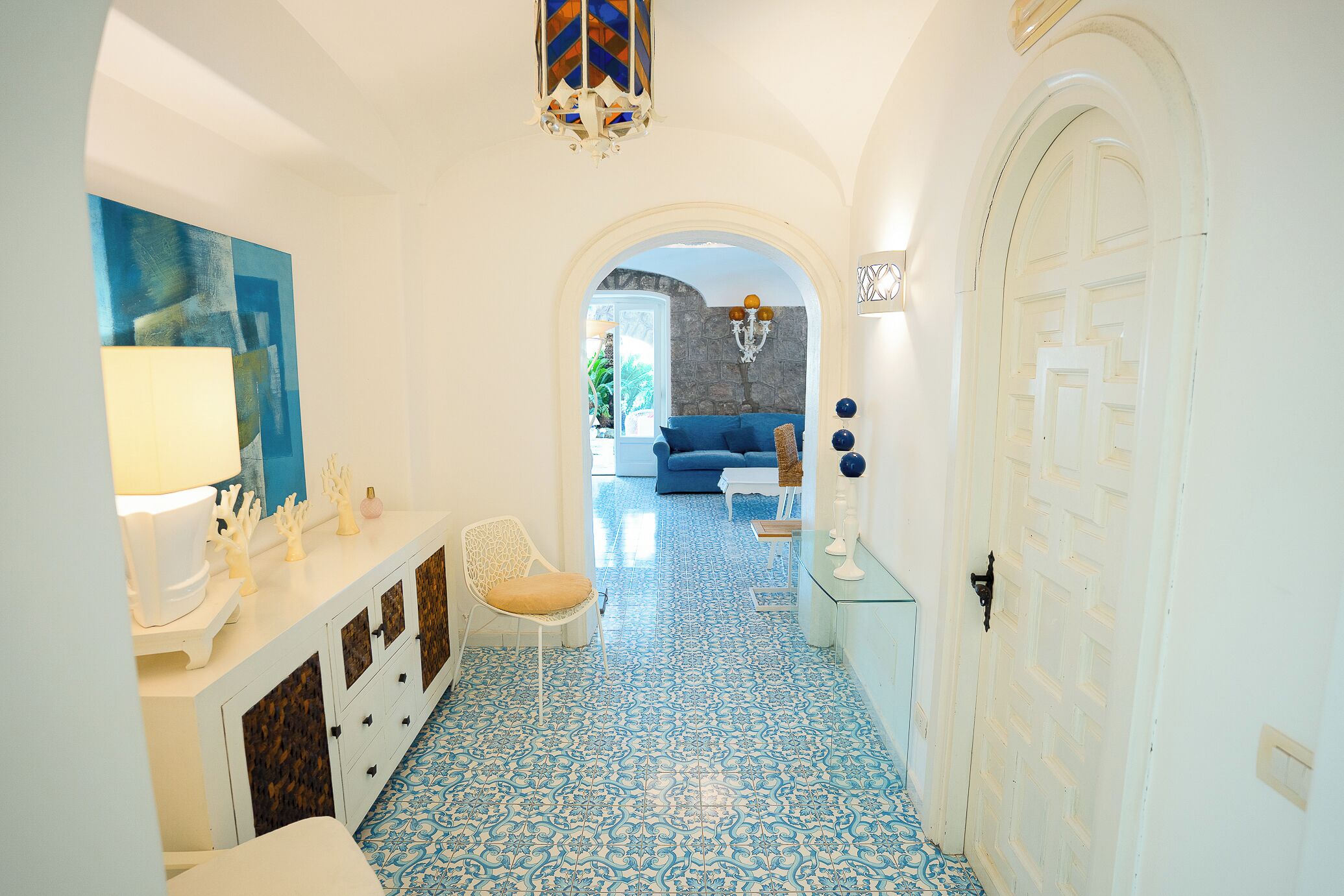 Un pasillo con suelo estampado, una puerta blanca y un sofá azul al fondo.