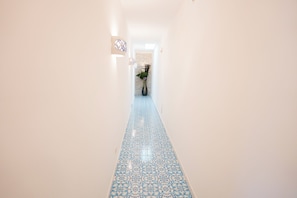 A hallway with a patterned floor, a potted plant, and a wall-mounted light fixture. - Villa Anna (Forio)