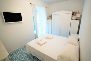 A hotel room with a bed, a TV mounted on the wall, a wardrobe, and a small table with a lamp. - Villa Anna (Forio)