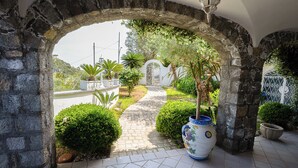 Ein Steinarches führt zu einem Garten mit einem gefliesten Weg, Blumentöpfen und einer Zierurne.