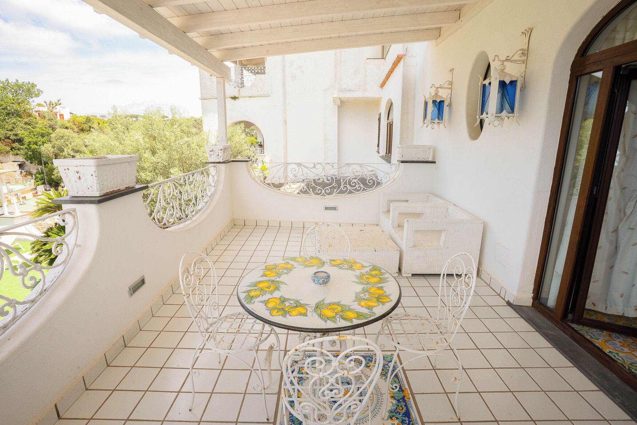 Un balcone con un tavolino rotondo, sedie in metallo bianco e una pianta in vaso.
