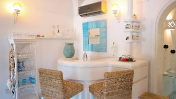Ein Badezimmer mit weißem Waschtisch, zwei Korbstühlen, einem Glastischchen mit Flaschen und einem spiegel mit blauer Rahmung.