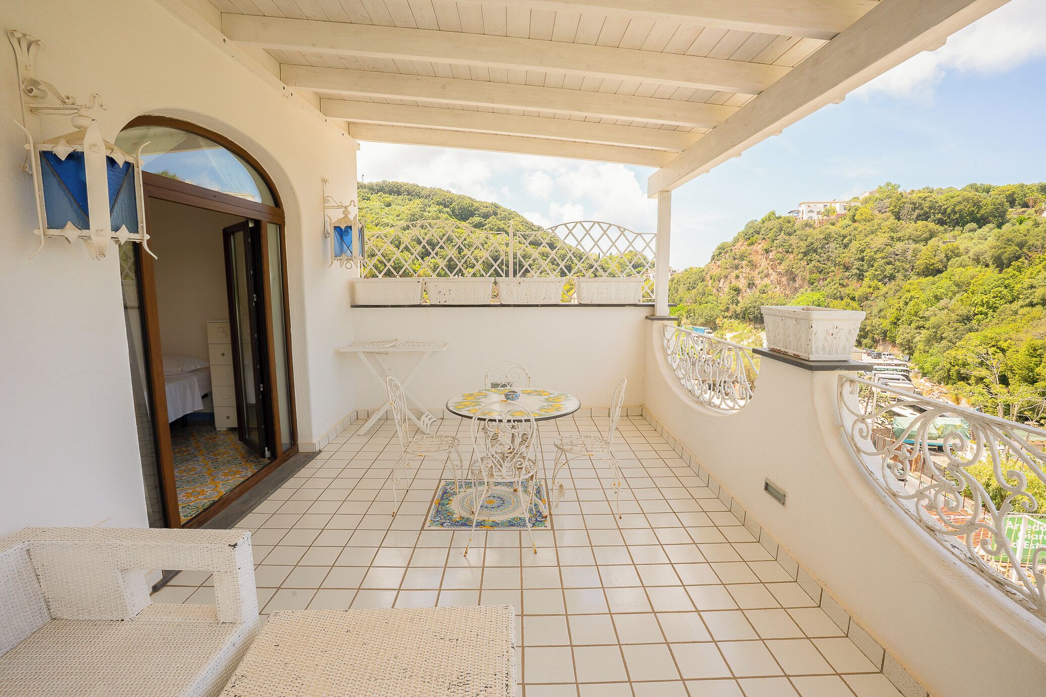 Ein Balkon mit Fliesenboden, einem kleinen Tisch mit Stühlen und Blick auf eine Hügelterrasse.