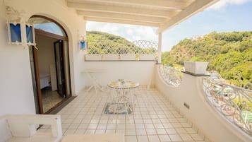 Ein Balkon mit Fliesenboden, einem kleinen Tisch mit Stühlen und Blick auf eine Hügelterrasse.