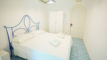 A neatly made bed with white linens and towels, a white wardrobe, and a patterned floor.