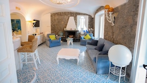 Ein Wohnzimmer mit Steinwand, Kamin, blau gemustertem Boden und einem runden weißen Tisch.