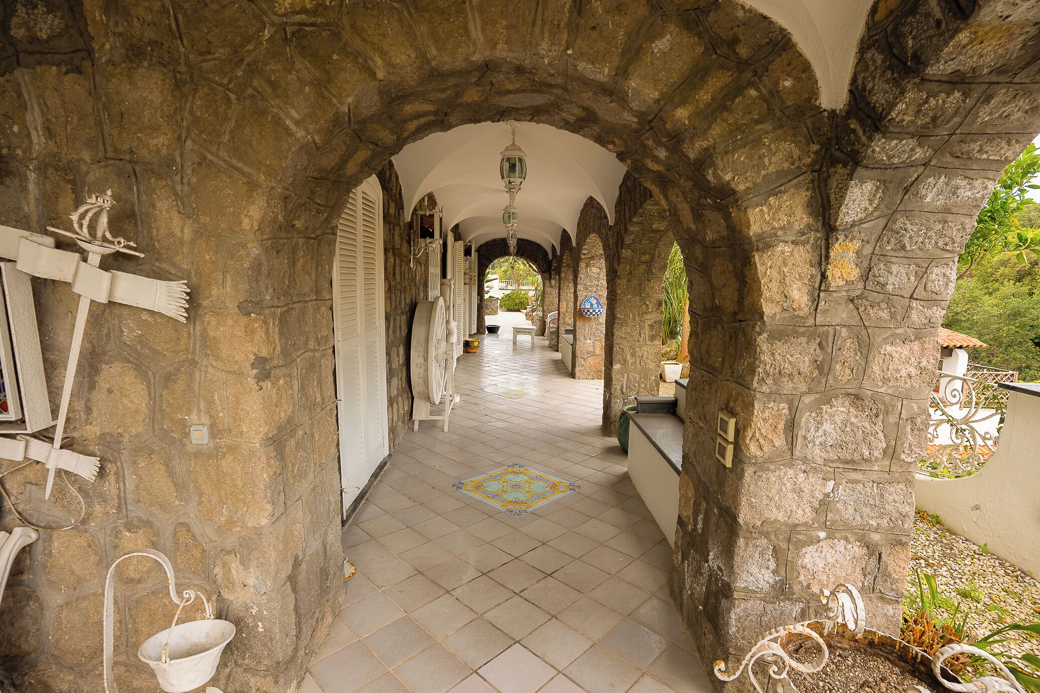 Un pasillo de piedra con arcos, suelo de baldosas y faroles colgantes.