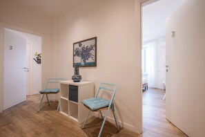 Ein Flur mit zwei blauen Stühlen, einem kleinen Tisch mit einer Vase und einem Bild an der Wand.
