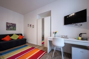 Ein modernes Wohnzimmer mit einem schwarzen Sofa, einem farbenfrohen Teppich, einem weißen Schreibtisch und einem Flachbildfernseher.