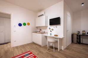 Eine kompakte Küche mit weißen Schränken, einer eingebauten Klimaanlage, einem kleinen Esstisch und einem an der Wand montierten Fernseher.