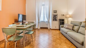 En matplats med ett bord och stolar, en tv, en soffa och ett fönster med gardiner.