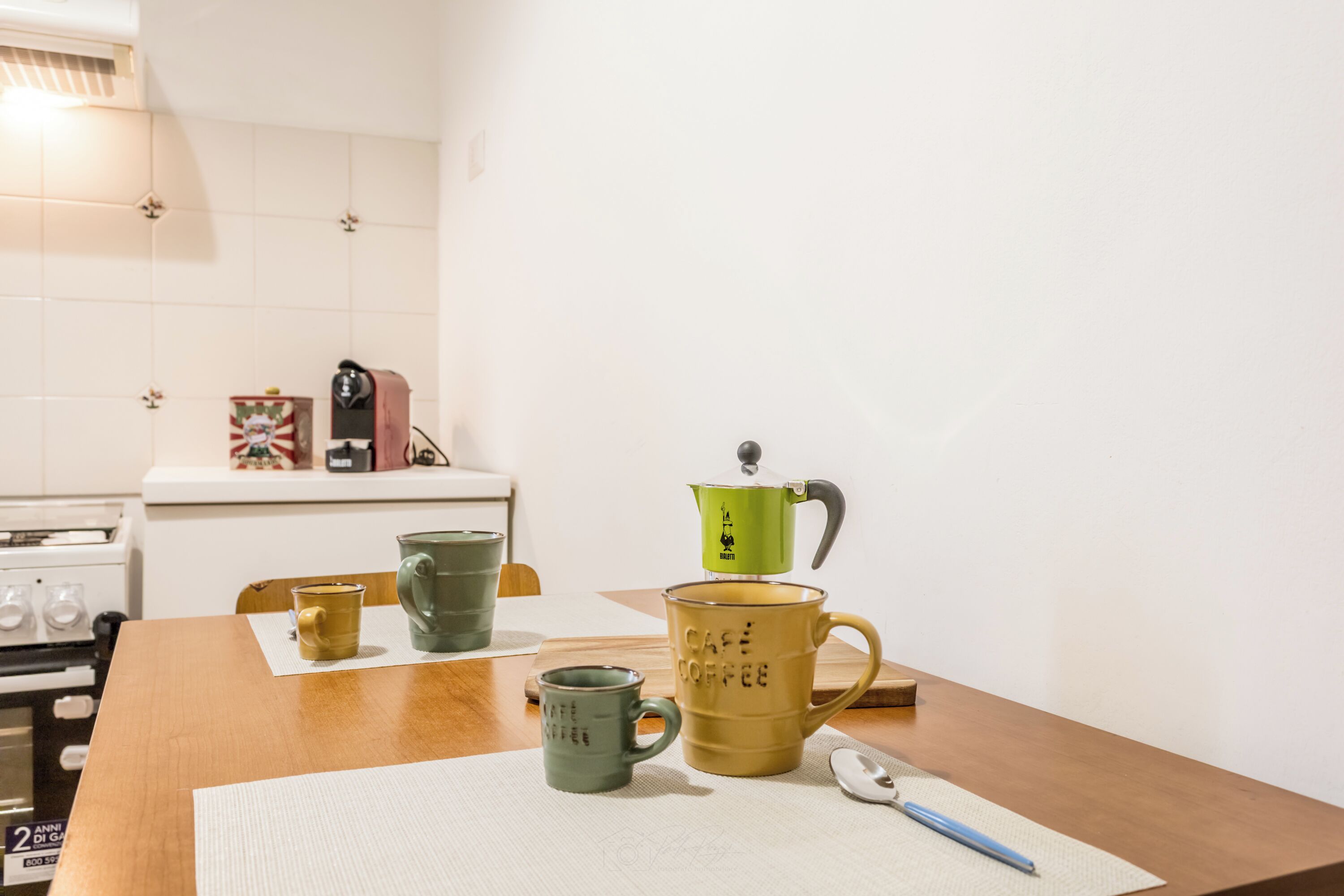 Una cocina con estufa, cafetera y varias tazas sobre la encimera.