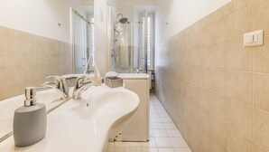 Ett modernt badrum med ett stort badkar, en dusch med glasväggar och en vit tvättställ med en tvålpump.