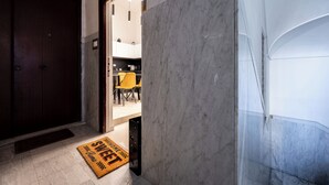 Un pasillo con suelo de mármol, una puerta de madera y una silla amarilla al fondo.