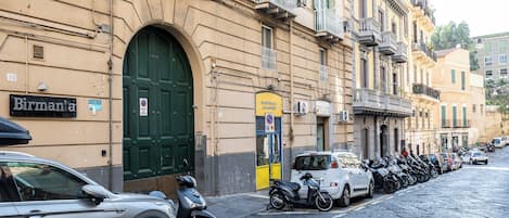 Una calle con autos y motocicletas estacionados, un edificio con una puerta verde y un letrero que dice 'Birmana'.
