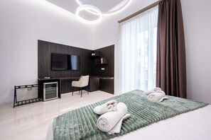 Ein modernes Hotelzimmer mit einem an der Wand befestigten Flachbildfernseher, einem Schreibtisch, einem Stuhl und einem Bett mit einer grün gemusterten Bettdecke.