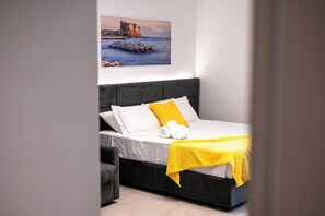 Une chambre à coucher moderne avec un lit, une tête de lit grise, un matelas blanc et un plaid jaune.