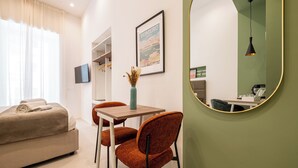 A modern hotel room with a bed, a dining area with a table and chairs, a framed picture on the wall, and a mirror on the wall.