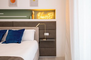 Ein ordentlich gemachtes Bett mit blauen und weißen Kissen, ein Nachttisch mit einer Lampe und ein Neon-Schild darüber.