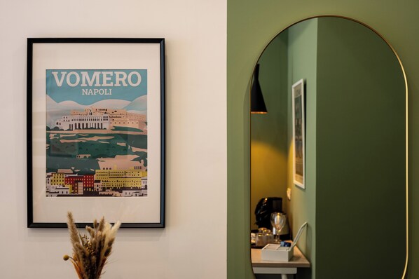 A framed cityscape poster, a mirror, and a small table with a coffee machine.