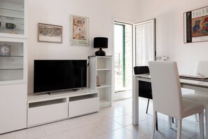 Una sala de estar moderna con televisor de pantalla plana, muebles blancos y obras de arte en las paredes.