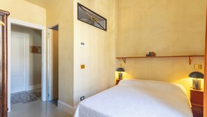A hotel room with a bed, two bedside lamps, a wall clock, and a door leading to another room. - Labicasa (Rome)