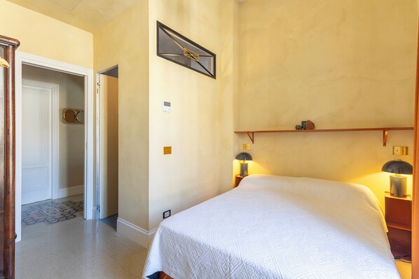 A hotel room with a bed, two bedside lamps, a wall clock, and a door leading to another room. - Labicasa (Rome)