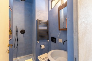 Ein Badezimmer mit blauer Wand, Waschbecken in Weiß, einem Handtuch, einer Duschbrause, einem Handtuchhalter und einem Spiegel.