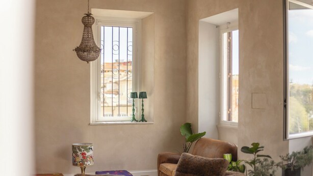 A living room with a sofa, a lamp, a potted plant, and a window with a view of buildings. - Labicasa (Rome)
