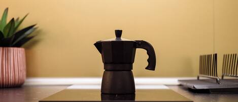 A coffee maker on a dark countertop with a potted plant and a radiator in the background.