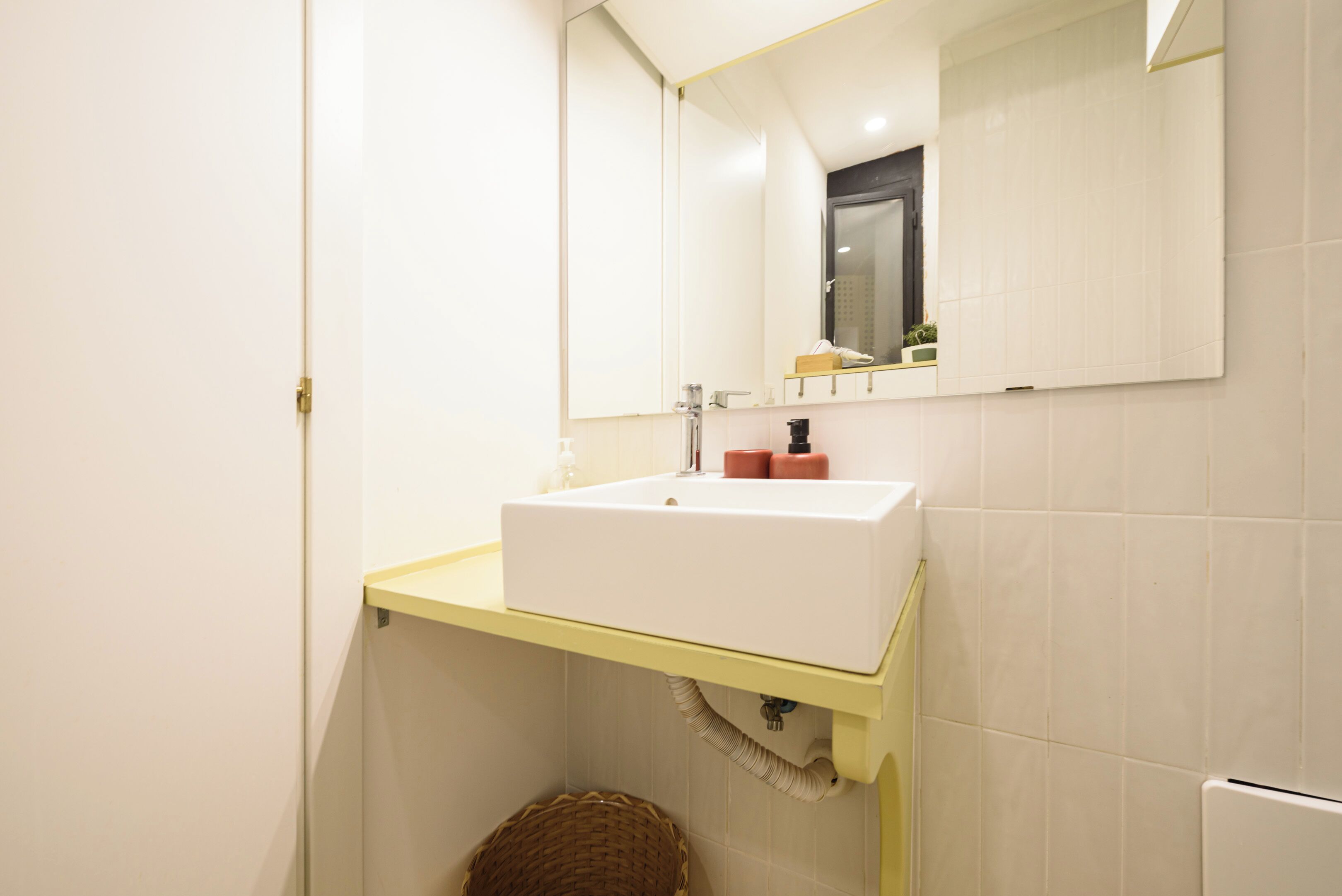 Un baño con un lavamanos blanco, encimera amarilla y un espejo encima.