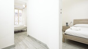 Une chambre à coucher au style minimaliste, avec un lit en bois, un banc et une fenêtre donnant sur des immeubles.