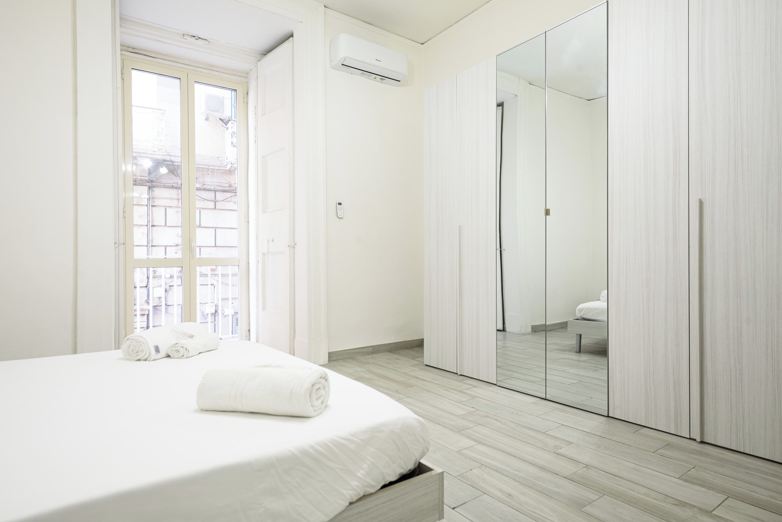A modern bedroom with a large bed, a walk-in closet, and a mirrored wardrobe.