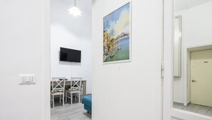 Une pièce avec un téléviseur fixé au mur, un tableau, une table à manger avec des chaises et un canapé bleu.