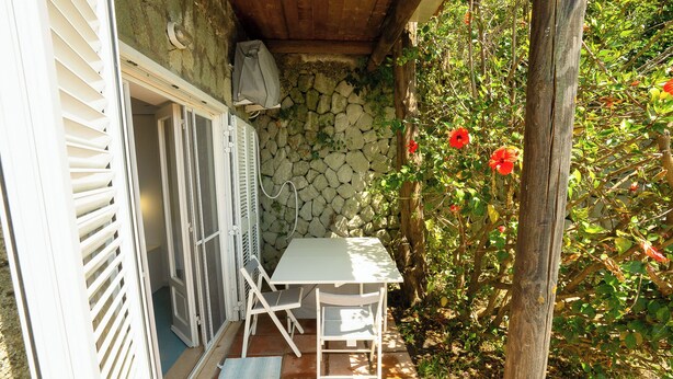 Une terrasse avec une table et des chaises, un mur en pierre et des fleurs rouges.