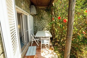 A patio with a table and chairs, a stone wall, and red flowers. - Villa La Pigrizia (Forio)