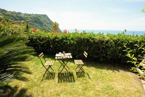 A grassy outdoor area with a table and two chairs, a palm tree, and a view of the sea and hills in the background. - Villa La Pigrizia (Forio)