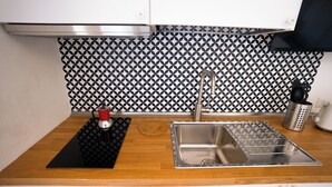 Une cuisine avec un évier en acier inoxydable, un tapis noir et une bouilloire rouge.