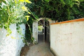 A narrow pathway leading to a gated entrance, surrounded by dense foliage and a white wall. - Villa La Pigrizia (Forio)