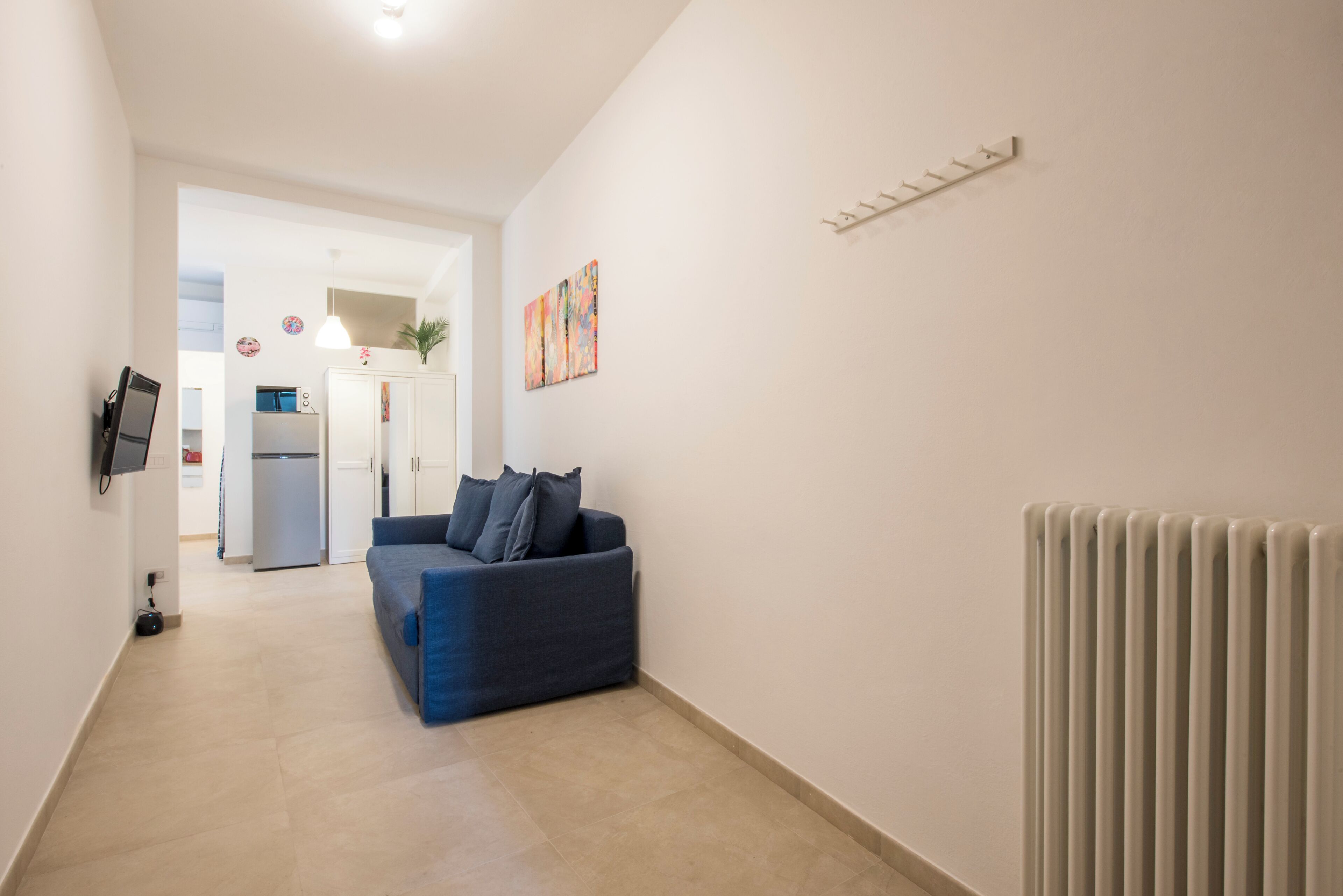 A hallway with a blue sofa, a radiator, and a kitchen in the background.