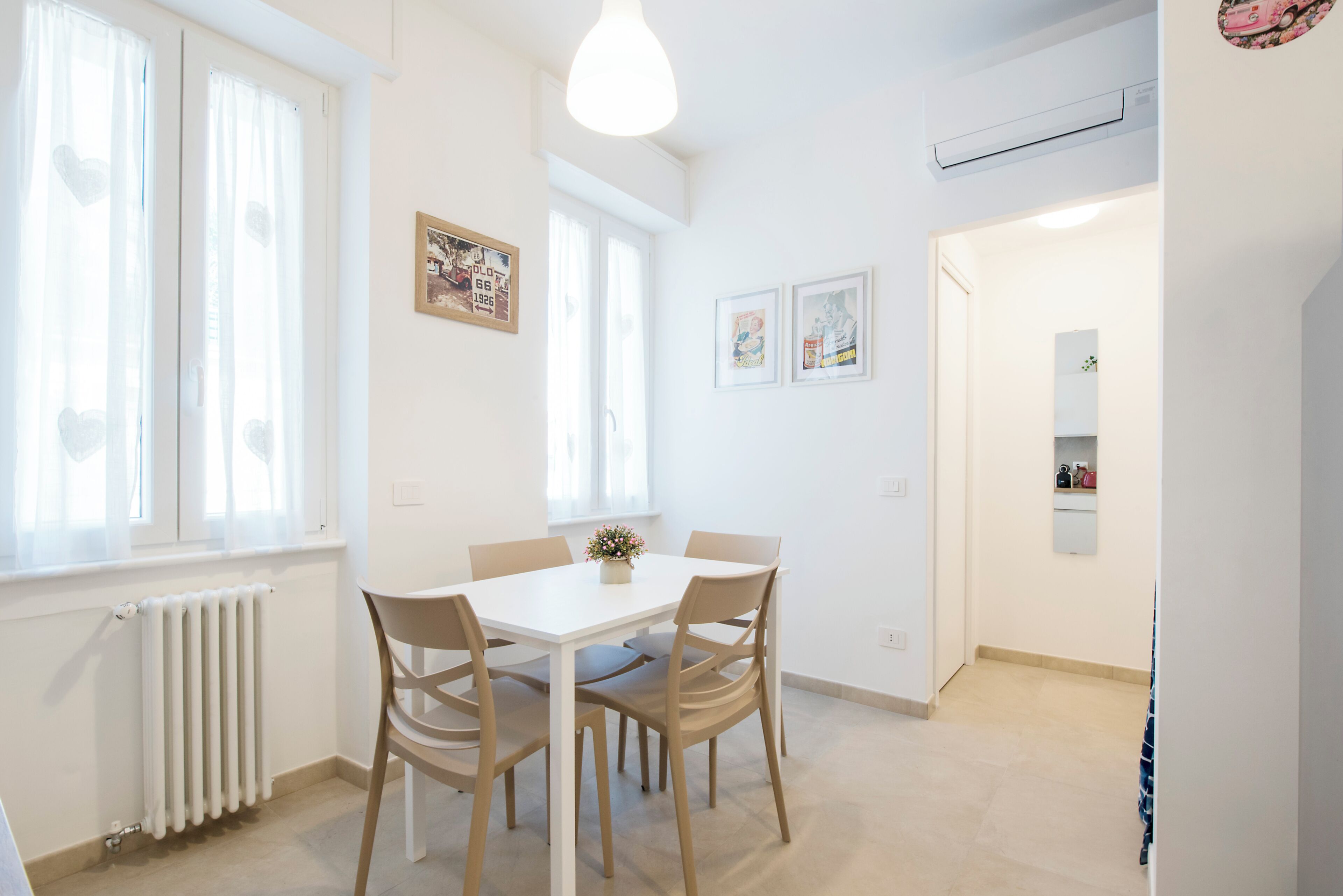 A dining area with a white table and four chairs, a radiator, and a ceiling light.