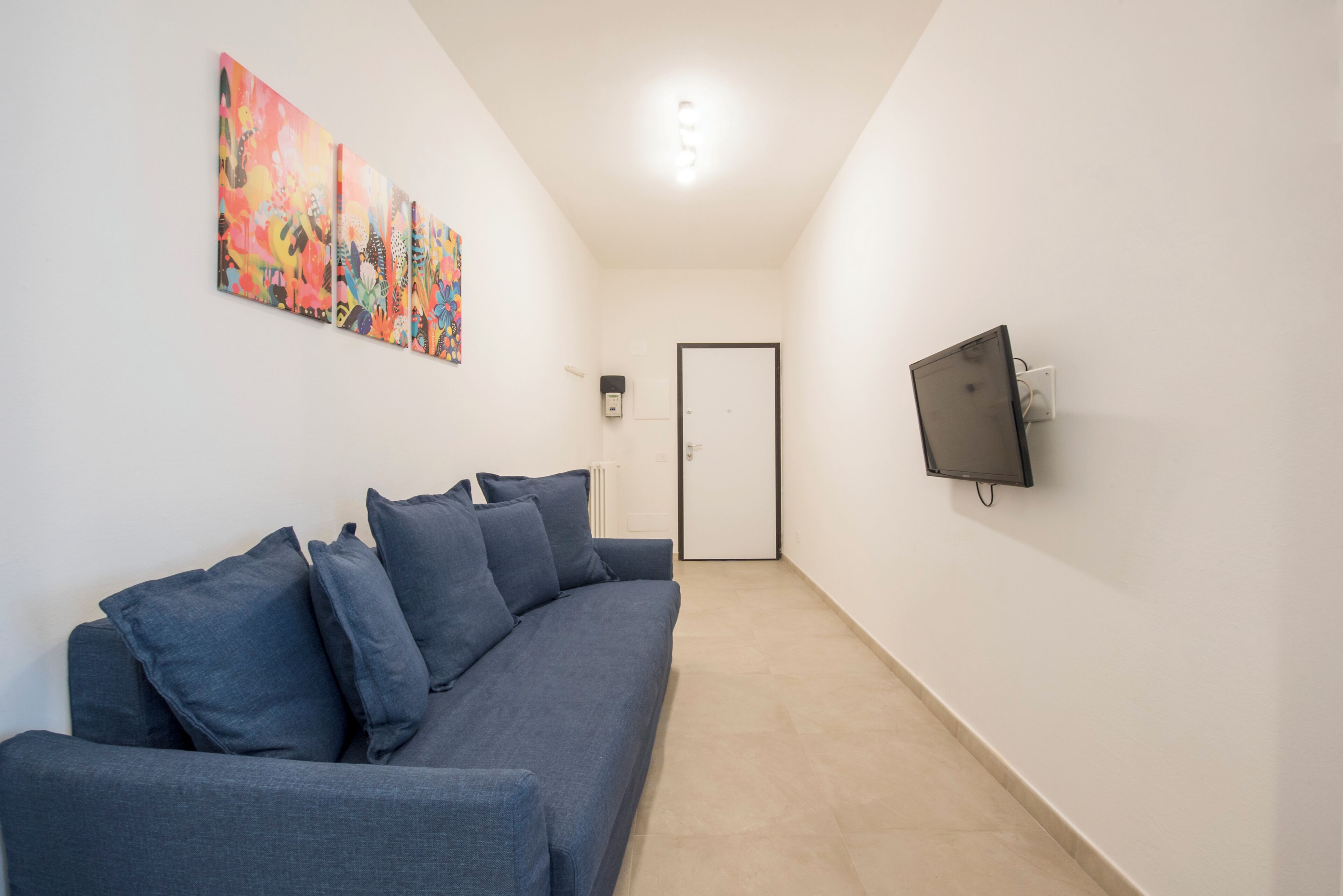 Ein modernes Wohnzimmer mit grauem Sofa, einem flachbildfernseher an der Wand und einem farbenfrohen abstrakten Gemälde über dem Sofa.
