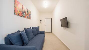 Ein modernes Wohnzimmer mit grauem Sofa, einem flachbildfernseher an der Wand und einem farbenfrohen abstrakten Gemälde über dem Sofa.