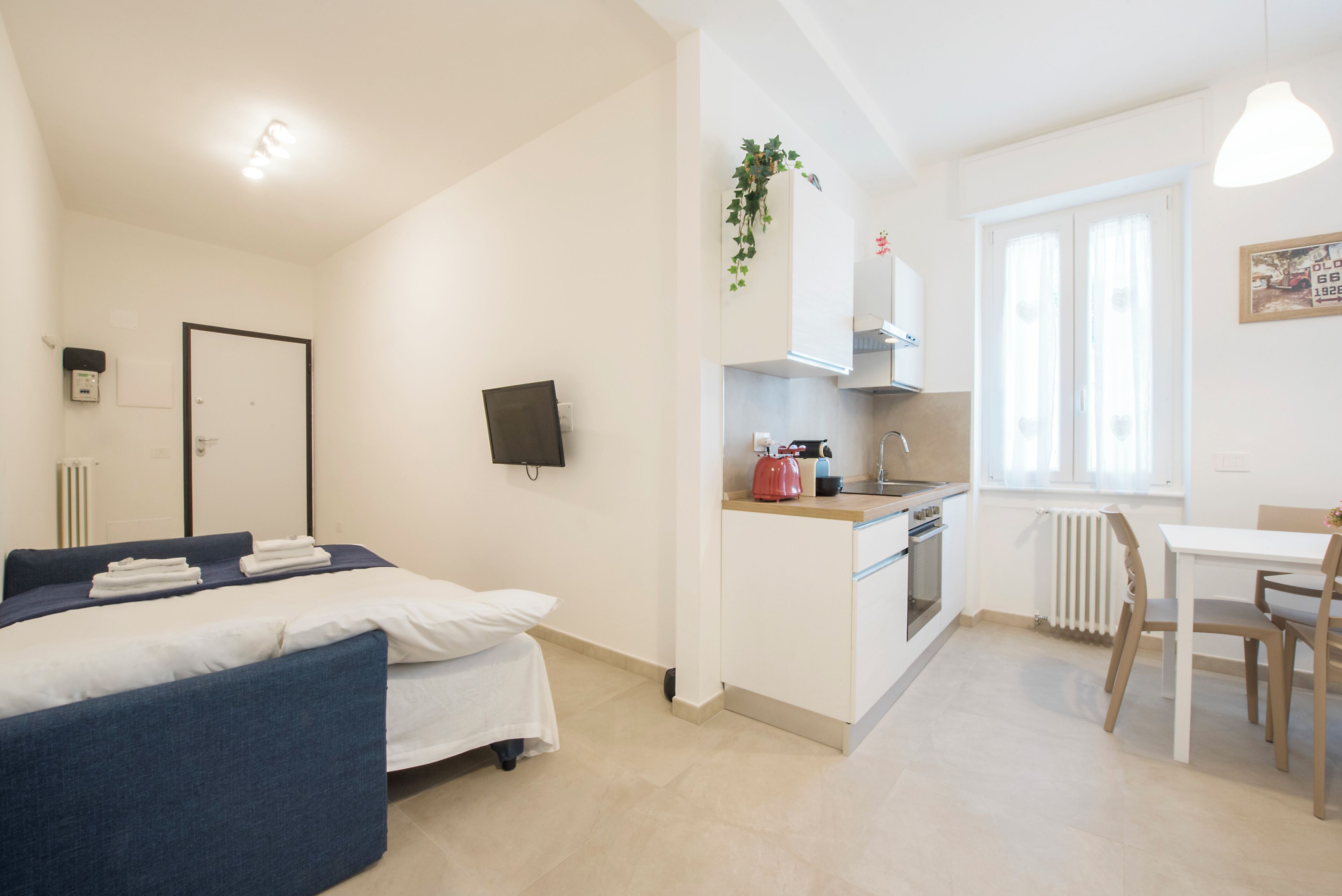 A compact hotel room with a bed, a kitchenette, a dining area, and a bathroom.